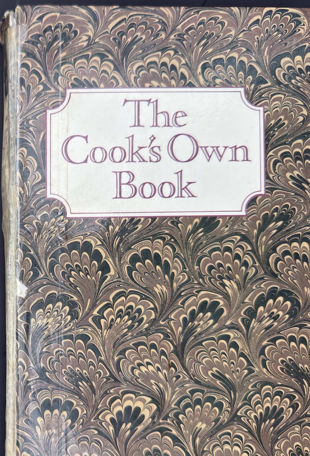 The Cook's Own Book, closed: a marbled brown cover with a cream label